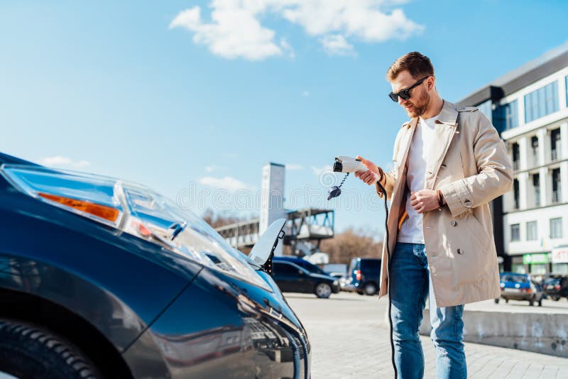 Casual man holds cable for charging electric car in his hand.