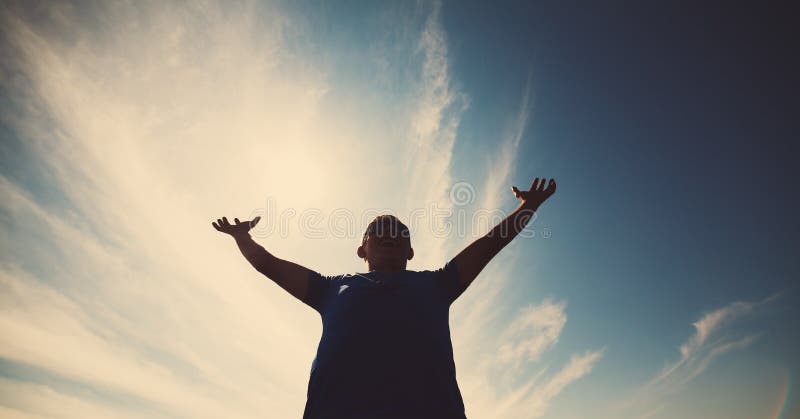 Casual man looking very happy with his arms up against blue sky in backlight . Young casual man gesturing success