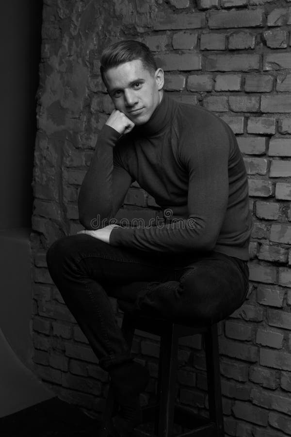 White Young Guy Sitting on a Chair Near a Gray Brick Wall, Black-and ...