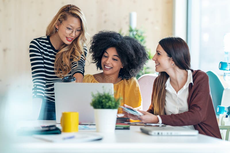 Casual multiethnic business women working with laptops while talking of they new projects together in coworking place