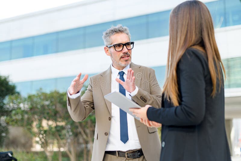 A senior businessman and a younger female colleague engage with content on a tablet together stock photography