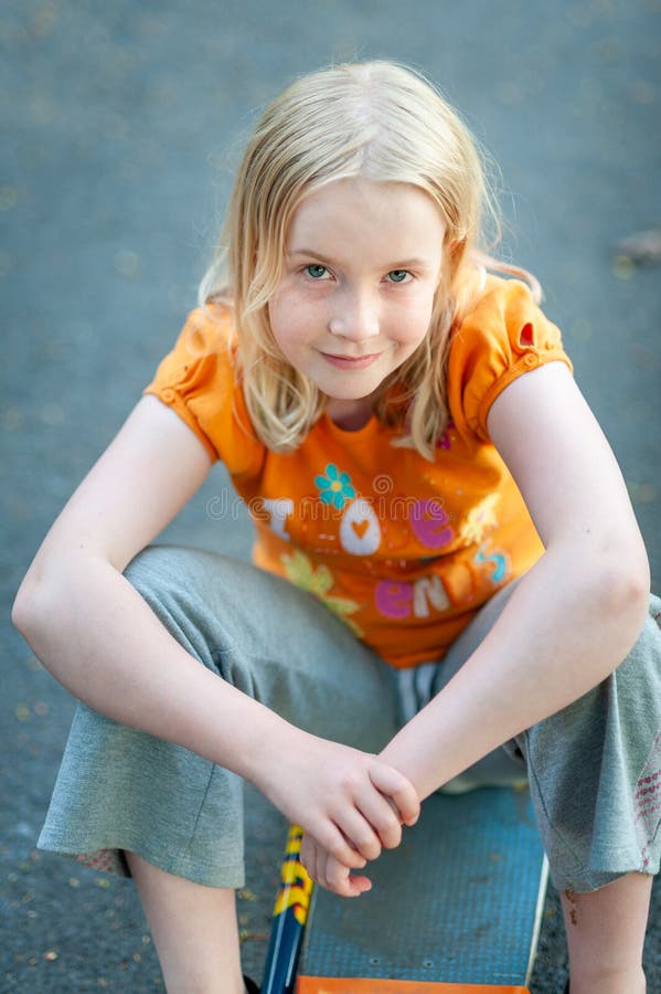 Casual Pretty Blonde Girl With Enigmatic Smile Sitting On A Skateboard