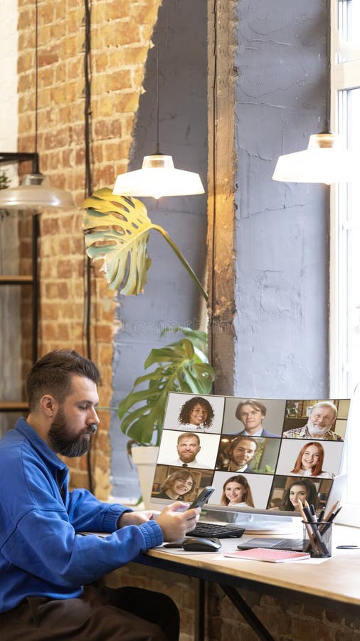 Casual worker in sweatshirt checking smartphone while attending remote meeting with colleagues displayed on screen royalty free stock photo