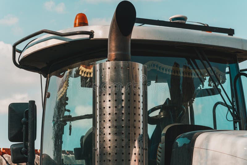 Catalytic converter tractor and cab with large windows close up on a background of blue sky. Exhaust pipe of a modern bulldozer