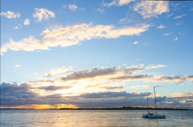 Catamaran sailboat in water at sunset with sun breaking though clouds on horizon royalty free stock images Catamaran sailboat in water at sunset with sun breaking though clouds on horizon royalty free stock images