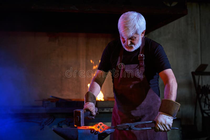 Caucasian Aged Blacksmith Hitting Molten Metal with Hammer Stock Image