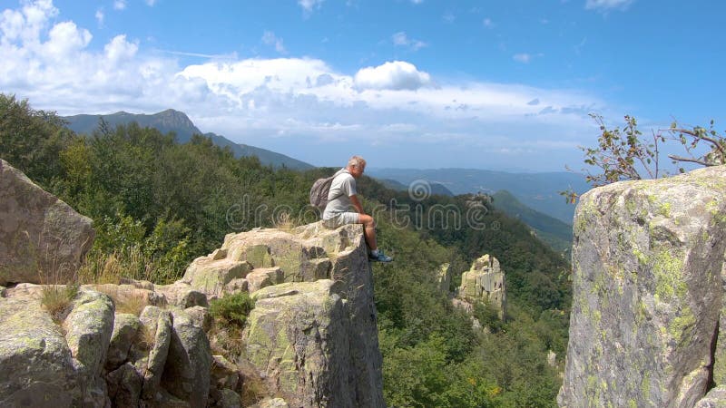 Caucasian blonde tourist man sitting on the rock in mountain Montseny in Spain over the valley with spectacular vista