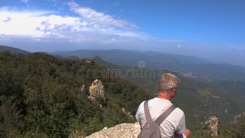 Caucasian blonde tourist man sitting on the rock in mountain Montseny in Spain over the valley with spectacular vista