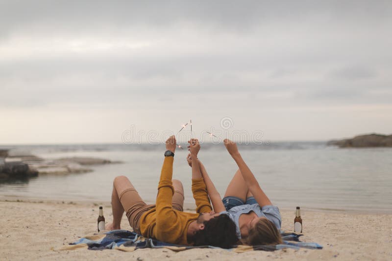 Caucasian couple playing with fire cracker while lying at beach stock photos Caucasian couple playing with fire cracker while lying at beach stock photos