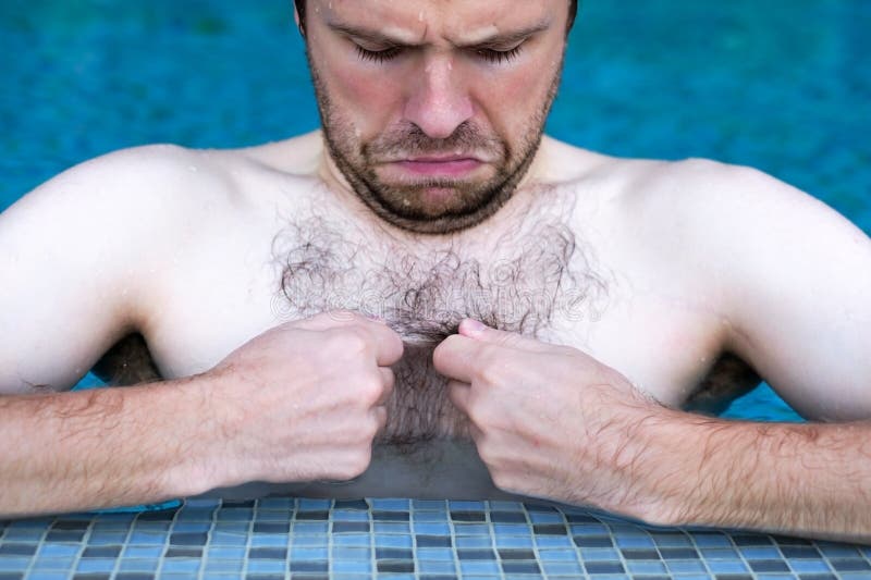 Caucasian dude swimming in pool. he is looking on his hair on chest with displeasure