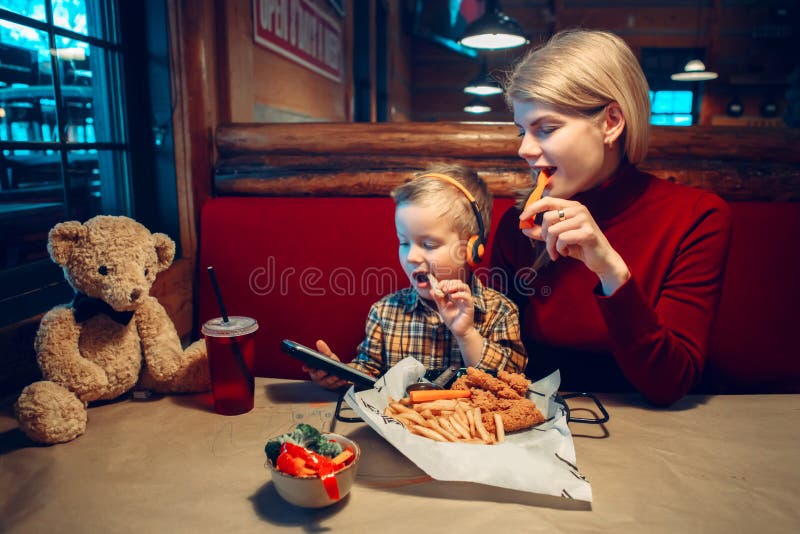 Mother and toddler boy son at restaurant. Caucasian family mother with toddler boy son eating food dinner in cafe restaurant and playing electronic digital royalty free stock photography