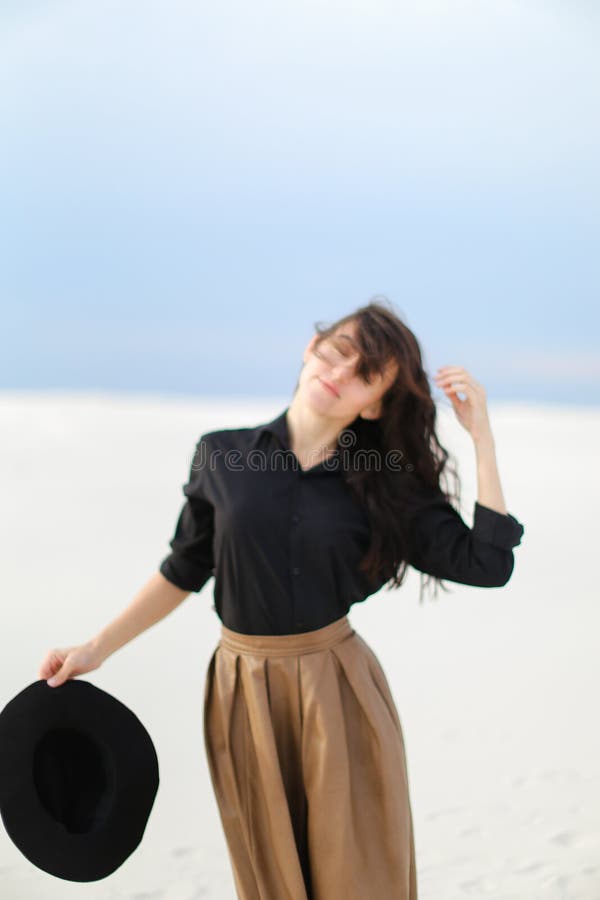 Caucasian female photo model standing on snow and wearing skirt and black blouse. keeping hat. stock photos