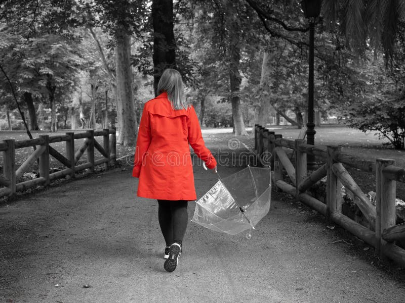 A Caucasian girl with a red gabardine walks through a park with a transparent umbrella in her hand royalty free stock images A Caucasian girl with a red gabardine walks through a park with a transparent umbrella in her hand royalty free stock images