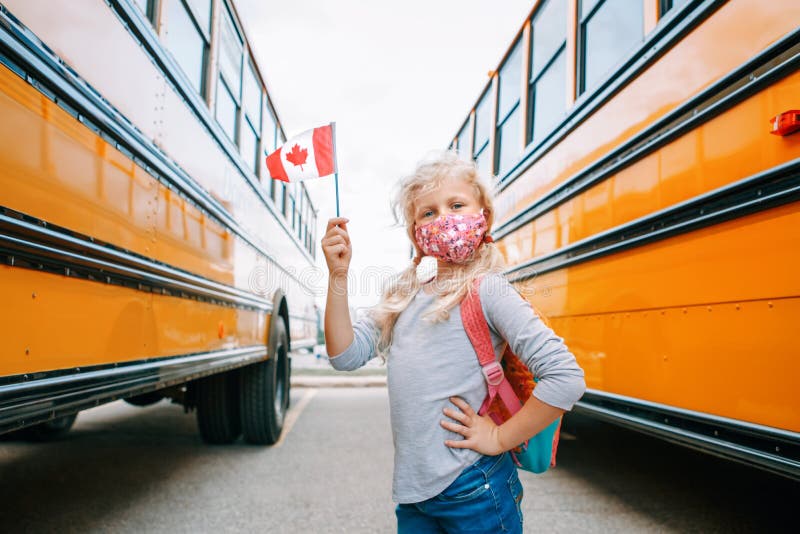 Caucasian girl student with face mask holding Canadian flag. Student kid near a yellow school bus in Canada. Education and back to royalty free stock photos Caucasian girl student with face mask holding Canadian flag. Student kid near a yellow school bus in Canada. Education and back to royalty free stock photos