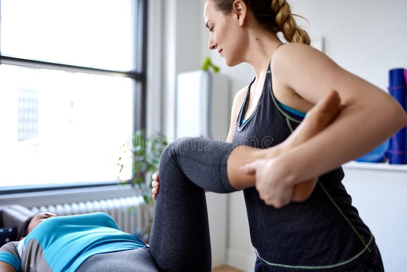 Caucasian kvinnafysioterapeut som strectching benet och knäet av mitt--vuxen människa en kinesisk kvinnlig patient som sitter på fotografering för bildbyråer Caucasian kvinnafysioterapeut som strectching benet och knäet av mitt--vuxen människa en kinesisk kvinnlig patient som sitter på fotografering för bildbyråer