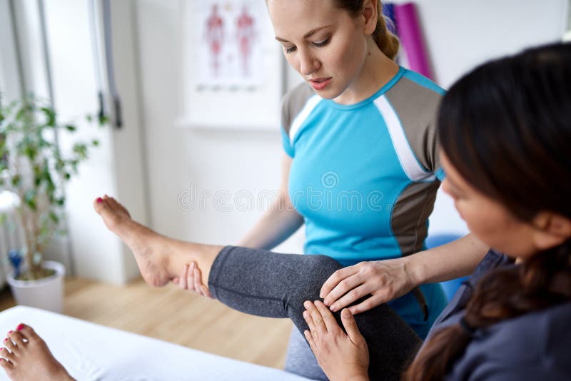 Caucasian kvinnafysioterapeut som strectching benet och knäet av mitt--vuxen människa en kinesisk kvinnlig patient som sitter på arkivfoton Caucasian kvinnafysioterapeut som strectching benet och knäet av mitt--vuxen människa en kinesisk kvinnlig patient som sitter på arkivfoton