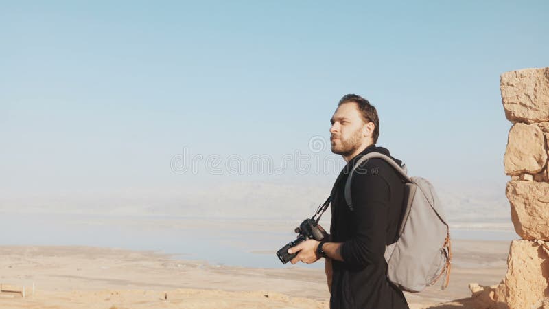 Caucasian man enjoys amazing Dead Sea panorama. Excited photographer stands on mountain top with camera Israel Masada 4K