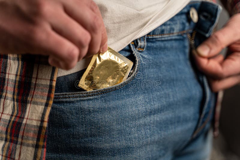 Caucasian man hand close-up takes out condom in gold package from jeans pocket. Sex theme with protection. Safe sex