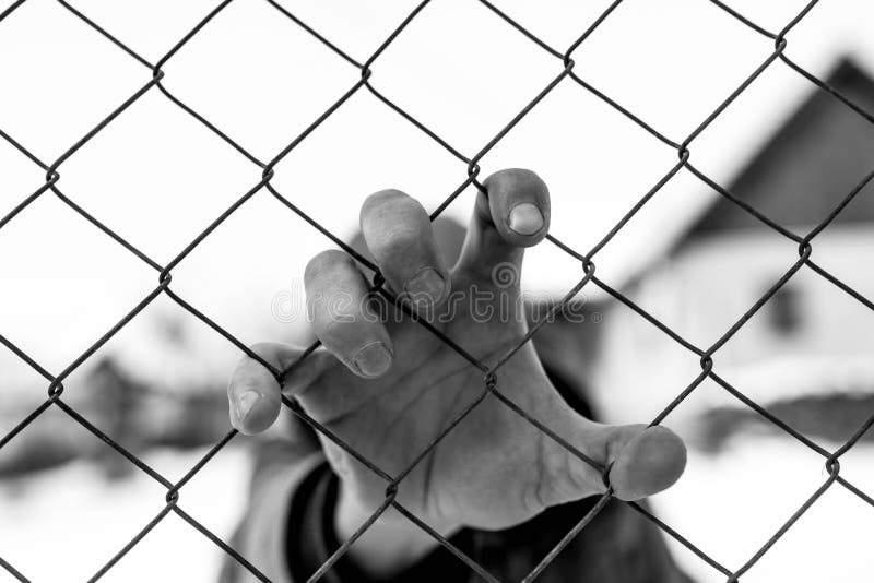 Caucasian man hand holding the wire fence at correctional institute in black and white.