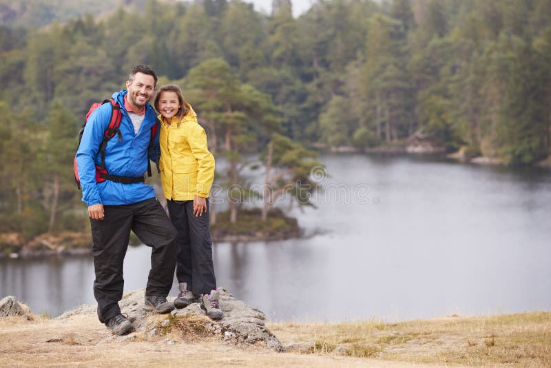 Caucasian pre-teen girl standing with her father on a rock by a lake, smiling to camera, lakeside background royalty free stock photography Caucasian pre-teen girl standing with her father on a rock by a lake, smiling to camera, lakeside background royalty free stock photography