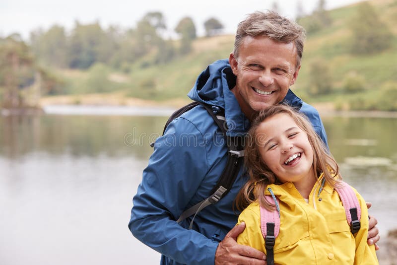 Caucasian pre-teen girl standing with her father on the shore of a lake, laughing at camera, close up