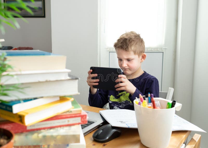Caucasian preteen boy play game on tablet instead of doing distance learning task. Books and copybooks around. Concept