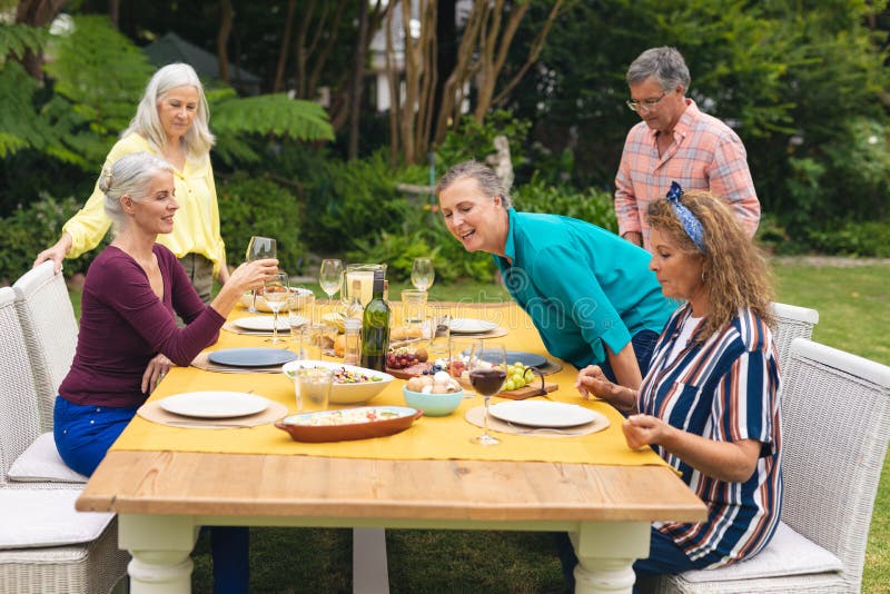 Caucasian senior male and female friends with food and wine at table in backyard
