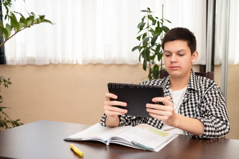 Caucasian teen boy learning language online using digital tablet, doing school tasks at home. E-learning concept