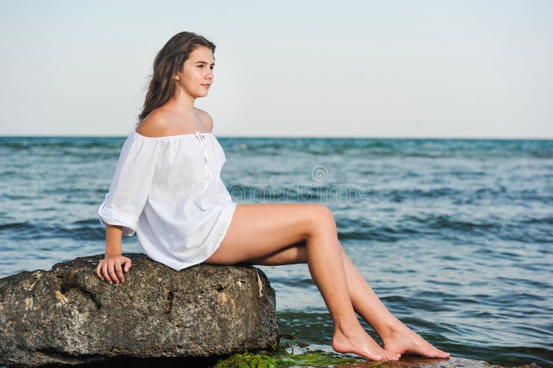 Caucasian Teen Girl In Bikini And White Shirt Lounging On Lava Rocks By 