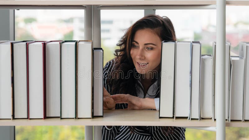 Caucasian woman at book shelf in library searching and reading book