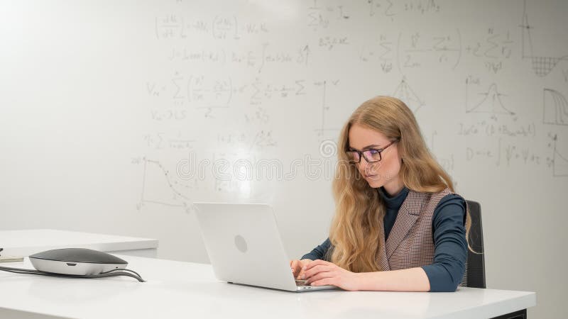 Caucasian woman scientist typing on laptop. White board with formulas. royalty free stock photo