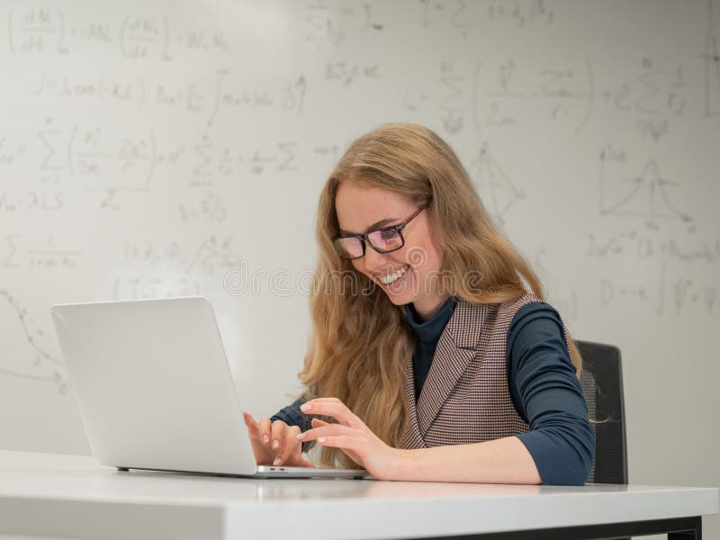 Caucasian woman scientist typing on laptop. White board with formulas. stock photo