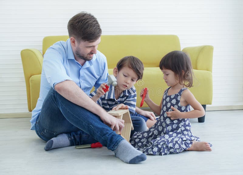 A Caucasian young father sitting on warm floor playing with happy little son and daughter