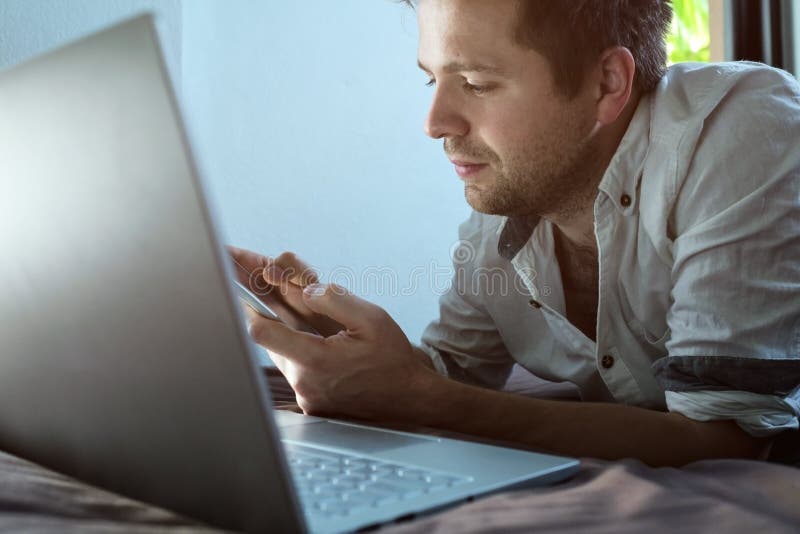 Caucasian young man lying on bed at his laptop. Working at home. royalty free stock photo Caucasian young man lying on bed at his laptop. Working at home. royalty free stock photo