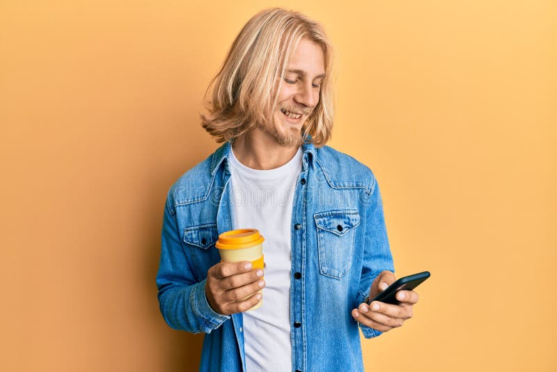 Caucasien jeune homme avec les cheveux longs en utilisant un smartphone et boire une tasse de café souriant avec un sourire heureu photos stock