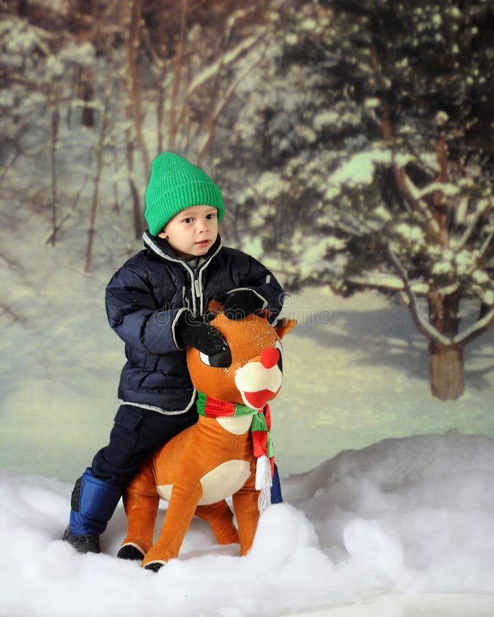 An adorable preschooler in the snow sitting on a large, toy Rudolph. An adorable preschooler in the snow sitting on a large, toy Rudolph.