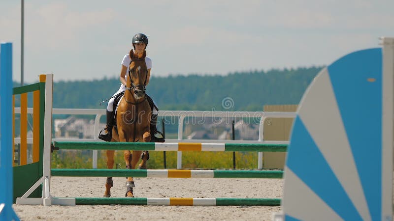 Há uma mulher montando um cavalo pulando sobre um obstáculo