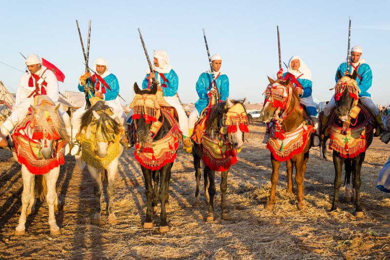 Photo taken in a Fantasia festival in Morocco. Moroccan men riding their horses and wearing proudly their traditional outfits to perform Fantasia. Fantasia is a traditional exhibition of horsemanship in the Maghreb performed during cultural festivals and to close Maghrebi wedding celebrations. `Fantasia` is an imported name, the actual traditional term used is lab el baroud `the gunpowder play`. The performance consists of a group of horse riders, all wearing traditional clothes, who charge along a straight path at the same speed so as to form a line, and then at the end of the charge about two hundred meters fire into the sky using old muskets or muzzle-loading rifles. The difficulty of the performance is in synchronizing the movement of the horses during acceleration of the charge, and especially in firing the guns simultaneously so that one single shot is heard. The horse is referred to as a fantasia horse and are of Arabian horse, Andalusian horse or Barb stock. The fantasia is considered a cultural performance and a kind of martial art; it also symbolizes a strong relationship between the man and the horse, as well as an attachment to tradition. Photo taken in a Fantasia festival in Morocco. Moroccan men riding their horses and wearing proudly their traditional outfits to perform Fantasia. Fantasia is a traditional exhibition of horsemanship in the Maghreb performed during cultural festivals and to close Maghrebi wedding celebrations. `Fantasia` is an imported name, the actual traditional term used is lab el baroud `the gunpowder play`. The performance consists of a group of horse riders, all wearing traditional clothes, who charge along a straight path at the same speed so as to form a line, and then at the end of the charge about two hundred meters fire into the sky using old muskets or muzzle-loading rifles. The difficulty of the performance is in synchronizing the movement of the horses during acceleration of the charge, and especially in firing the guns simultaneously so that one single shot is heard. The horse is referred to as a fantasia horse and are of Arabian horse, Andalusian horse or Barb stock. The fantasia is considered a cultural performance and a kind of martial art; it also symbolizes a strong relationship between the man and the horse, as well as an attachment to tradition.