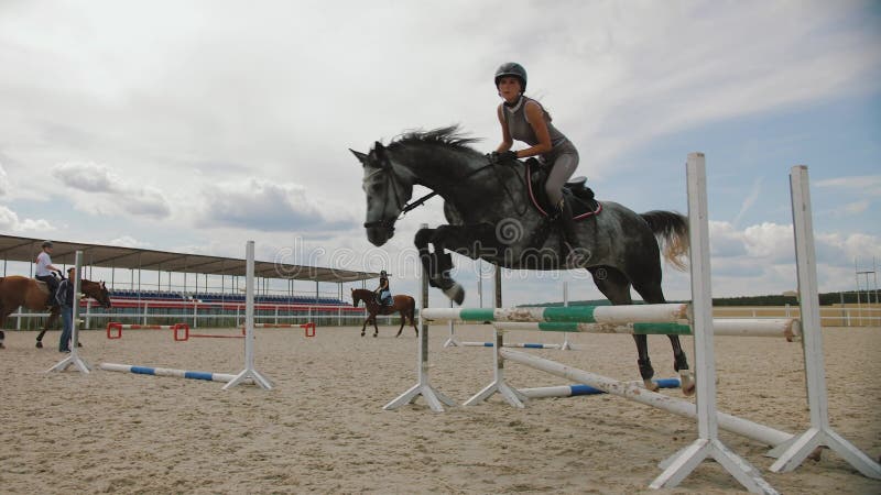 Há uma mulher montando um cavalo pulando sobre um obstáculo