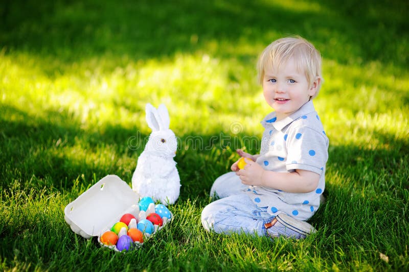 Caza del niño pequeño para el huevo de Pascua en jardín de la primavera el día de Pascua fotografía de archivo Caza del niño pequeño para el huevo de Pascua en jardín de la primavera el día de Pascua fotografía de archivo