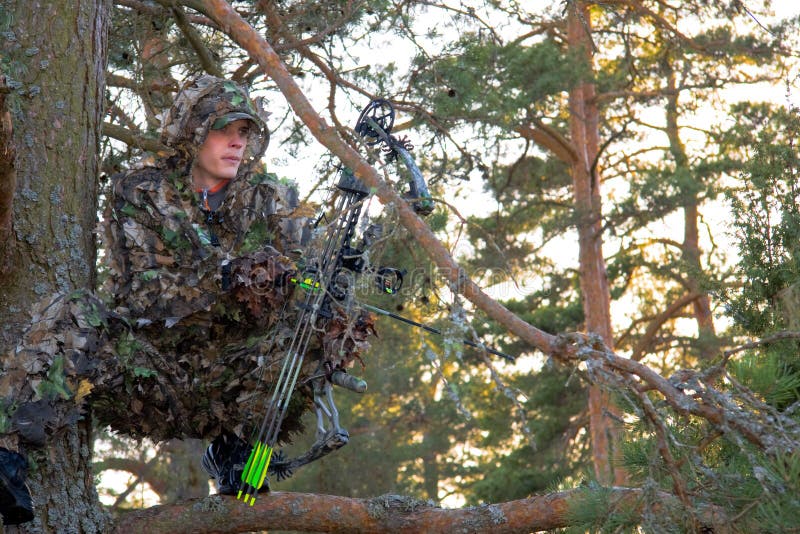 Bow hunter shouting for game, sitting on a branch in the forest. Bow hunter shouting for game, sitting on a branch in the forest