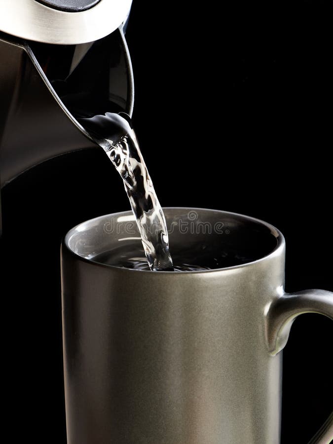 Ceainicul modern care toarnă apă în cupă izolată pe negru stock image