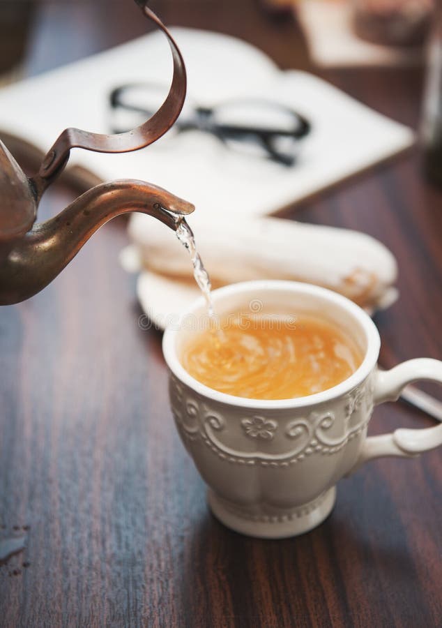 Ceainică de cupru de calitate veche, turnând ceai pe masă de lemn stock image