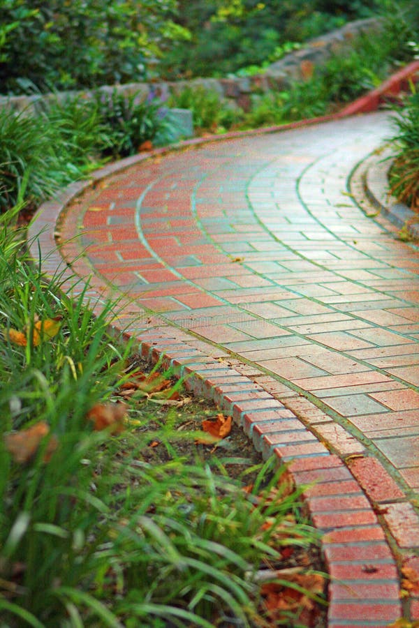 A beautifully lit, curved brick path meanders through a gorgeous garden lined with plants and flowers. A beautifully lit, curved brick path meanders through a gorgeous garden lined with plants and flowers.