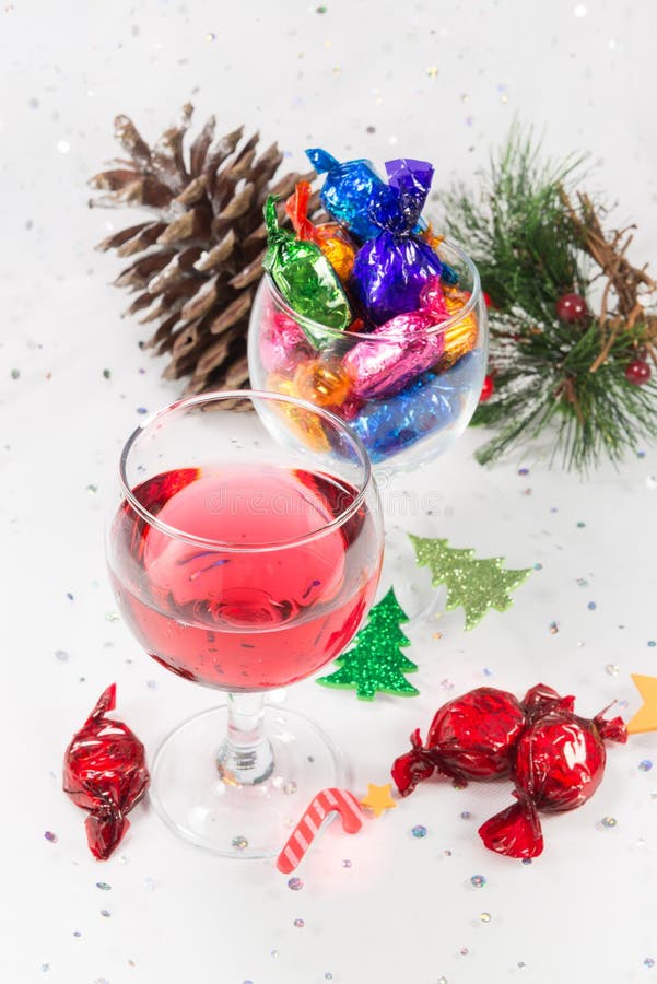 Festive Christmas party celebrations with glass of wine and wrapped chocolate candy sweets. Treats to enjoy the merry holiday season. On a snowy white background. Festive Christmas party celebrations with glass of wine and wrapped chocolate candy sweets. Treats to enjoy the merry holiday season. On a snowy white background.