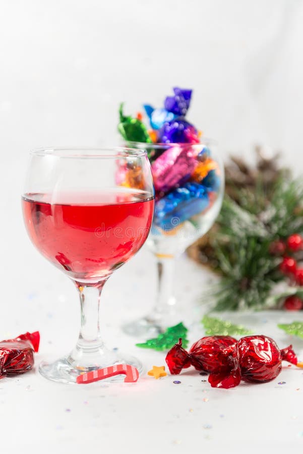 Christmas party celebrations with wine and wrapped chocolate candy sweets. Treats to enjoy the merry holiday season. on a snowy white background. Vertical. Christmas party celebrations with wine and wrapped chocolate candy sweets. Treats to enjoy the merry holiday season. on a snowy white background. Vertical.