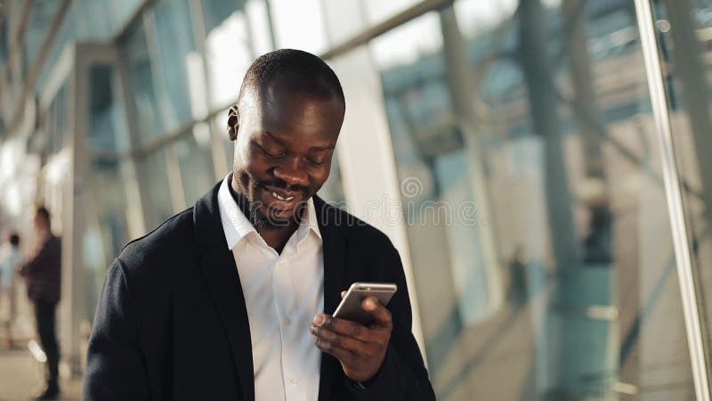 Celebración que anima del hombre de negocios afroamericano feliz mirando el teléfono celular y sosteniendo una gran cantidad de d