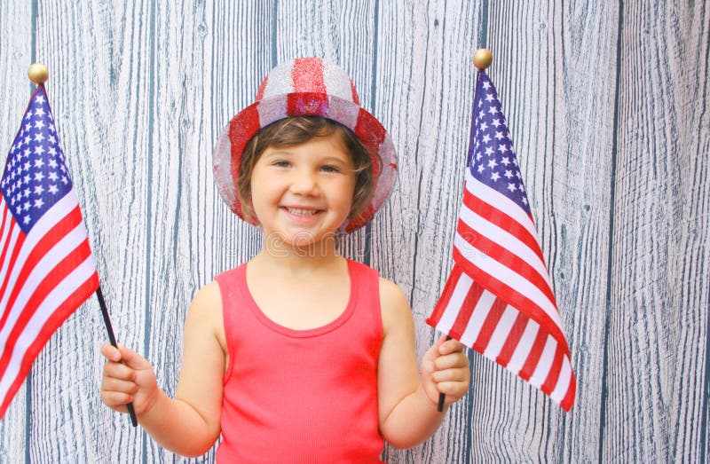 Young girl wearing 4th of july hat and holding two flags in celebration. Young girl wearing 4th of july hat and holding two flags in celebration