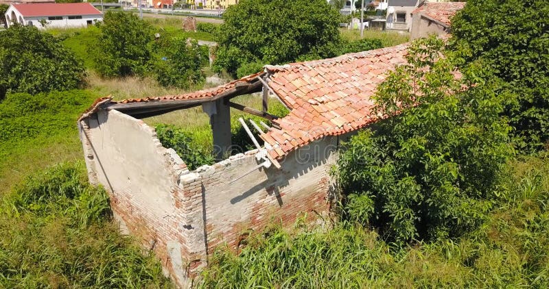 Celeiro velho com telhado arruinado em jardim verde negligenciado