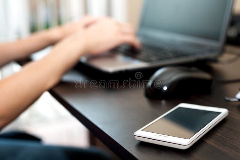 Cell phone (smartphone) on a table and woman working on the laptop computer